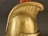 gold helmet on a stand with a red pom pom on top