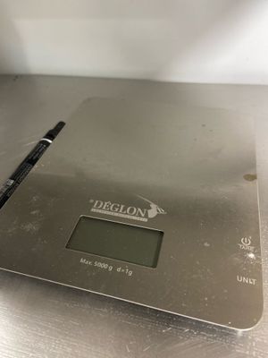 silver electronic scale with a pen on top of it on a table