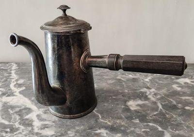 une cafetière en argent avec une poignée en bois, posée sur une table en marbre