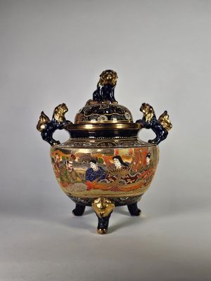 un vase doré et noir muni d'un couvercle, posé sur un socle