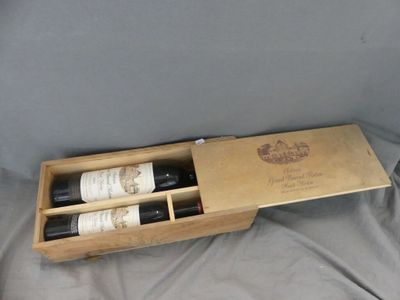 two bottles of wine in a wooden box on a bed