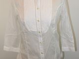 La chemise est blanche et possède un col boutonné.