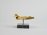 une image représentant un avion doré posé sur un socle en marbre noir