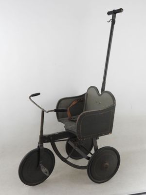 une petite poussette jouet noire avec des roues posée sur une surface blanche