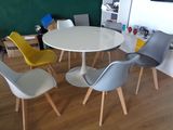 Des chaises aux couleurs vives sont disposées autour d'une table ronde blanche dans une pièce