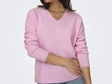 a woman wearing a pink sweater and jeans stands in front of a white background