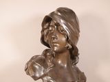 bronze bust of a woman with a hat on her head