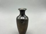 un petit vase en métal posé sur une surface blanche