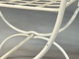 a white metal bench with a basket on top of it