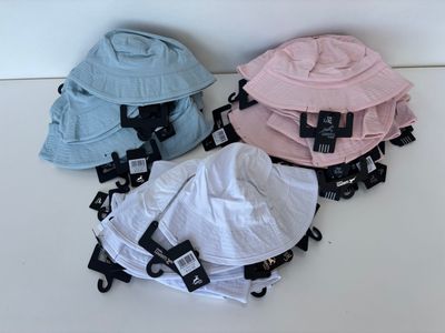 Plusieurs chapeaux sont alignés sur une surface blanche, accompagnés d'étiquettes noires.