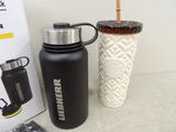 a black and silver water bottle next to a white vase