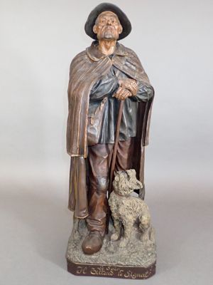 statue représentant un homme coiffé d'un chapeau et vêtu d'une cape, tenant un chien dans ses bras