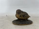 un petit oiseau en bronze posé sur un socle en bois