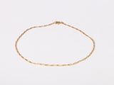 a gold chain bracelet with a tiny bead on a white surface