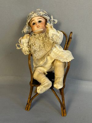 une petite poupée assise sur une chaise, coiffée d'un chapeau