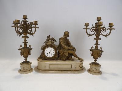 une statue représentant un homme assis sur une table, à côté de trois chandeliers