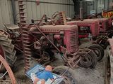 many old tractors in a barn with a man standing next to them