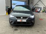 the front end of a grey car in a garage with a large screen on the wall