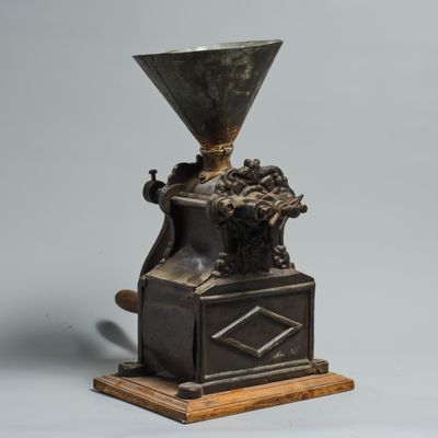 un moulin à café ancien posé sur un socle en bois, sur fond gris