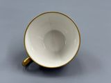 une tasse à café blanche et dorée posée sur une surface grise