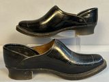 une paire de sabots en cuir noir exposés sur une surface blanche