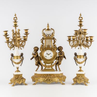 une horloge en or posée sur une table, à côté de trois lustres