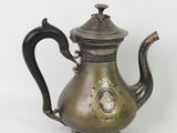une théière ancienne en laiton, avec un couvercle et une anse, sur fond blanc