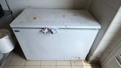 a white refrigerator in a dirty kitchen with a trash can