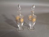 two clear glass vases with gold designs on them sitting on a table