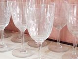 several empty wine glasses lined up on a shelf in front of a wallpapered wall