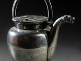 une vieille théière en argent avec une anse, posée sur une table