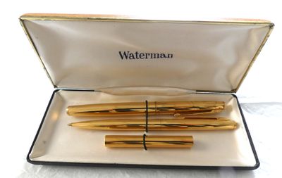 trois stylos à plume dorés dans un étui posé sur une surface blanche
