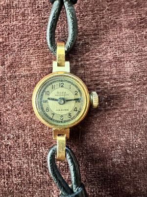 une photo d'une montre-bracelet en or posée sur un tissu marron