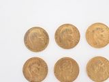 six gold sovereigns of different sizes and shapes on a white surface