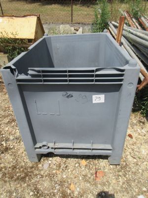 un conteneur gris posé par terre à côté d'un tas de tuyaux métalliques