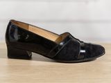 the black shoes are on a wooden table near a white wall