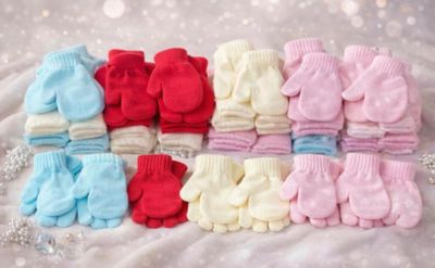 many pairs of baby mittens on a white blanket