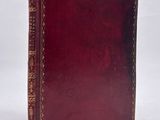 an old book with a red cover sitting on a white surface