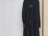 Le manteau est suspendu à un portant, près d'un mur blanc.