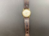 a gold watch with a brown leather band on a black surface