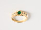 gros plan d'une bague en or avec une pierre verte et des diamants