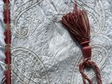 a close up of a white and red pillow with a tassel on it