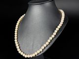a pearl necklace on a mannequin stand against a black background