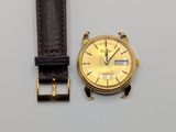 une montre en or avec un bracelet en cuir marron posée sur une surface blanche