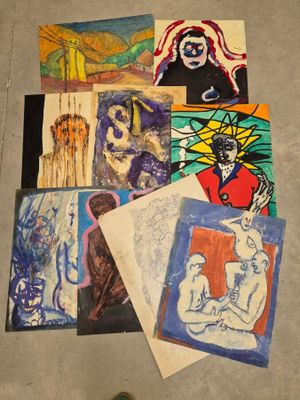 de nombreux tableaux posés à même le sol d'une pièce, avec une personne debout à côté d'eux
