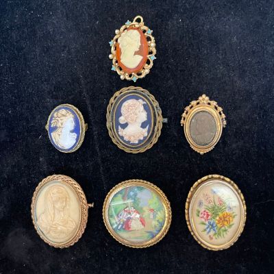 six miniature cameos are displayed in a gold frame on a black surface