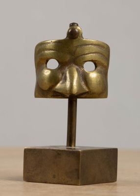 une photo représentant un masque en bronze posé sur un socle, lui-même posé sur une table en bois