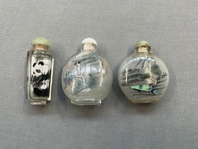 trois flacons à tabac en verre décorés de peintures, posés sur une table