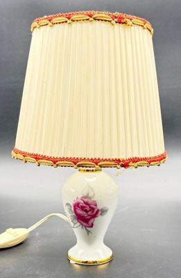a white lamp with a pink rose on it next to a lamp shade