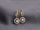 une paire de boucles d'oreilles en or et diamants posées sur un tissu gris